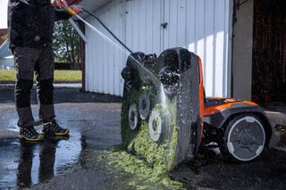Asmuo, žarna valantis roboto vejapjovės apačią, pašalinantis žolės šiukšles.