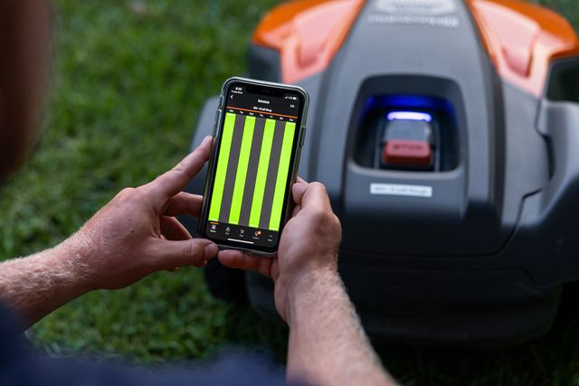 Una persona che utilizza un'app per smartphone per controllare un robot tagliaerba in un giardino.