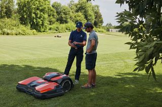 芝生の上に立ってロボット芝刈り機について話し合う2人。