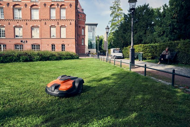 Robot cortacésped funcionando en un césped bien cuidado frente a un edificio histórico de ladrillos.