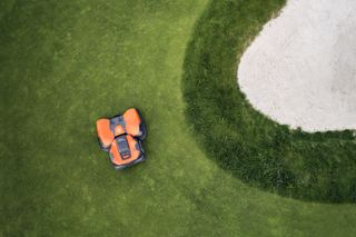 Kosiarka robotyczna pracująca na polu golfowym w pobliżu bunkra z piaskiem.