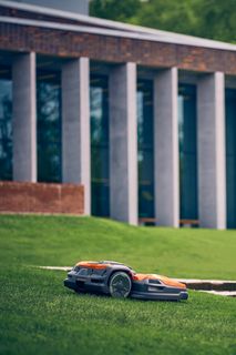 Ρομποτικό χλοοκοπτικό που λειτουργεί σε χλοοτάπητα κοντά σε ένα σύγχρονο κτίριο.