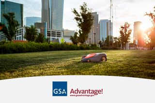 Robotic lawn mower operating on a city lawn with skyscrapers in the background.