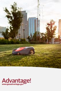 Robotic lawn mower operating on a city lawn with skyscrapers in the background.