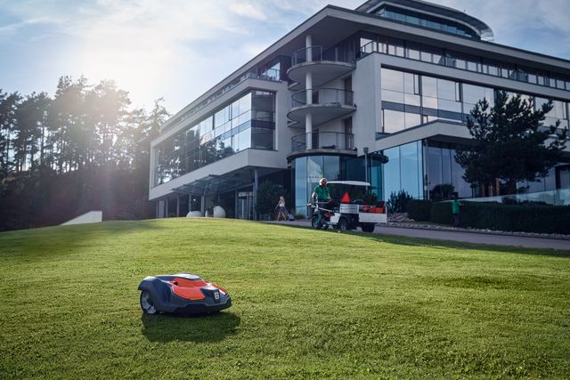 A robotic lawn mower operating on a well-maintained lawn in front of a modern building.