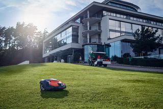 Un robot tondeuse fonctionnant sur une pelouse bien entretenue devant un bâtiment moderne.