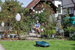 Robotic lawn mower operating in a garden with a house in the background.