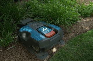 Robotic lawn mower operating in a garden with a satellite signal icon overlay.
