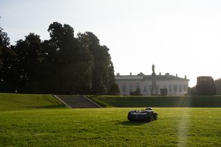 Robot tagliaerba al lavoro in un grande giardino con un edificio storico sullo sfondo.