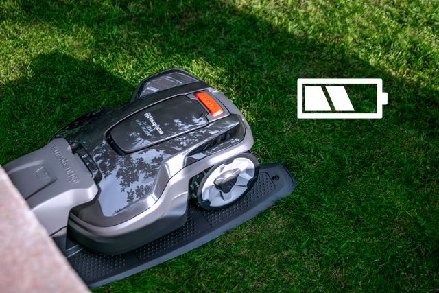 Robotic lawn mower operating in a garden with a battery level icon overlay.