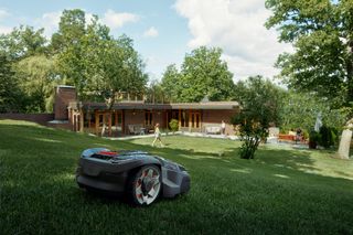 Robot cortacésped funcionando en un jardín con una casa moderna al fondo.