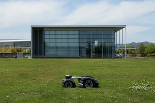 モダンなガラス張りの建物の前の開けた芝生で、昼間、ロボット芝刈機。