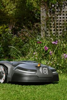 Robot cortacésped funcionando en un jardín con flores de colores.