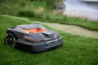 Robotic lawn mower operating on a grassy area near a water body.