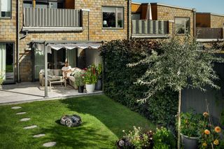Een robotmaaier die werkt in een goed onderhouden tuin met een persoon die ontspant op een terras.
