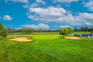 Una vista panoramica di un campo da golf con bunker di sabbia e un laghetto sotto un cielo nuvoloso.