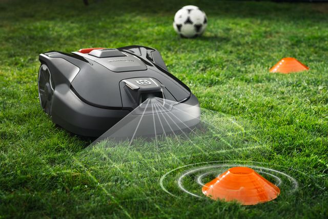 Robotska kosilica radi u vrtu s nogometnom loptom i čunjevom u blizini.