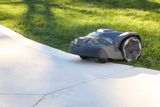 Robotic lawn mower navigating along the edge of a concrete path in a garden.