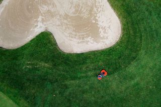 Aerial top view of a robotic lawn mower cutting grass near a sand bunker on a golf course.