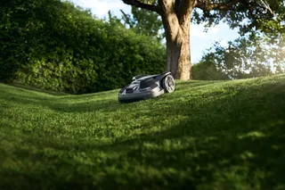Robotic lawn mower operating on a grassy slope in a garden.