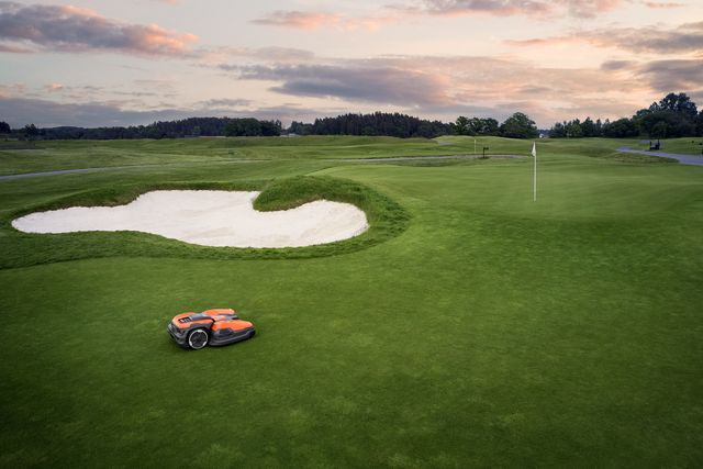Kosiarka robotyczna pracująca na polu golfowym w pobliżu bunkra z piaskiem.