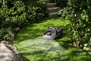 A robotic lawn mower operating on a well-maintained garden lawn with surrounding greenery.