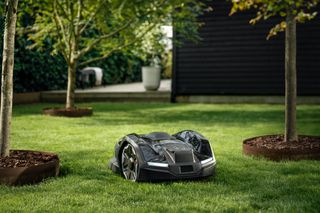 Robotic lawn mower operating in a garden surrounded by trees.