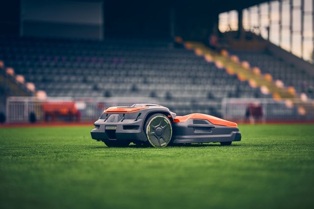 Mähroboter auf einem Sportplatz mit Stadionsitzen im Hintergrund.