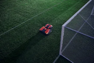 Robotmaaier die op een voetbalveld in de buurt van een doelpaal werkt.