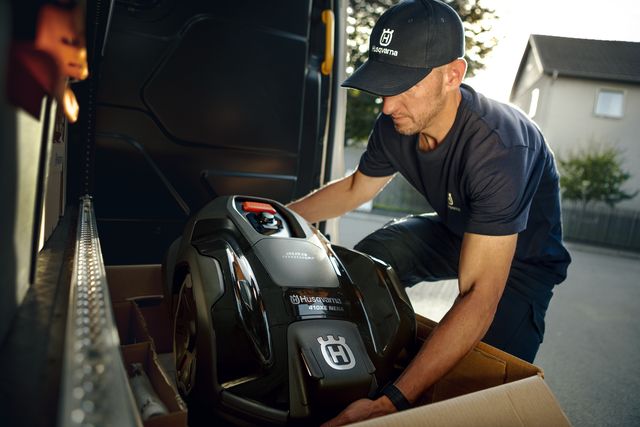 Eine Person, die einen Husqvarna Mähroboter in ein Fahrzeug setzt.