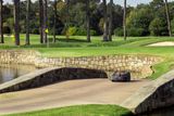 Robotic lawn mower crossing a stone bridge on a golf course.