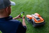 A person using a smartphone to control a robotic lawn mower on a grassy lawn.