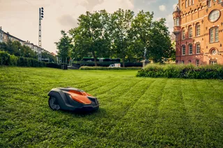 Robotic lawn mower operating on a neatly trimmed lawn beside a historic building.