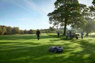 Un robot tondeuse fonctionnant sur un parcours de golf avec des personnes à l’arrière-plan.