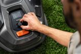 En person som justerar inställningarna på en Husqvarna robotgräsklippare i en trädgård.