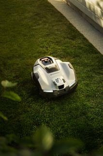 Robotic lawn mower operating on a grassy lawn beside a wooden fence.