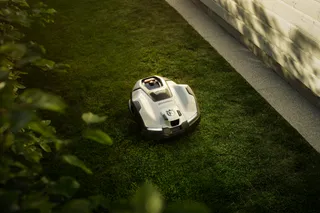 Robotic lawn mower operating on a grassy lawn beside a wooden fence.