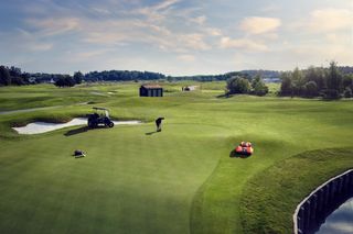 En person som spelar golf på en golfbana med en robotgräsklippare som sköter greenen.