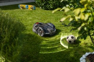 Robotic lawn mower navigating around a soccer ball in a garden.