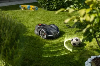 Robotska kosilica za travu koja se kreće oko fudbalske lopte u bašti.