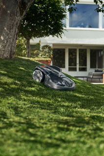 Robotic lawn mower operating on a grassy slope in a garden.