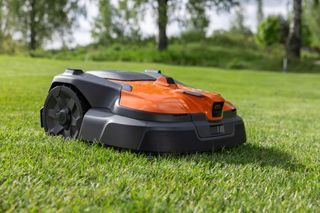 Robotic lawn mower operating on a well-maintained lawn with trees in the background.