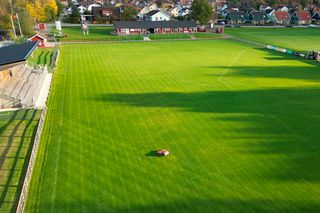 Un robot tondeuse fonctionnant sur un grand terrain de football bien entretenu.