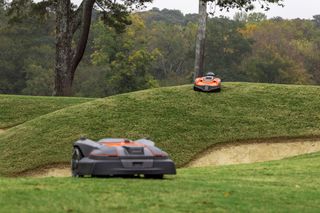 Two robotic lawn mowers operating on a hilly golf course.