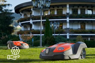 Zwei Mähroboter, die auf einer Rasenfläche vor einem großen Gebäude mit einem Einstellungssymbol arbeiten.