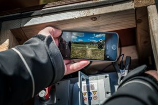 A person taking a photo of a lawn with a smartphone, near a battery with clamps attached.