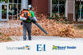 A person using a leaf blower to clear fallen leaves in an urban setting.