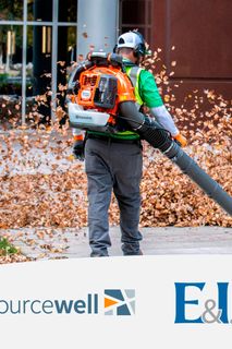 A person using a leaf blower to clear fallen leaves in an urban setting.