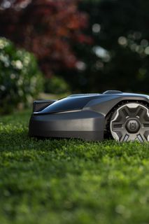 Robotic lawn mower operating on a grassy lawn with blurred background.