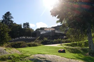 Robô corta-relva a funcionar numa encosta relvada num jardim soalheiro.